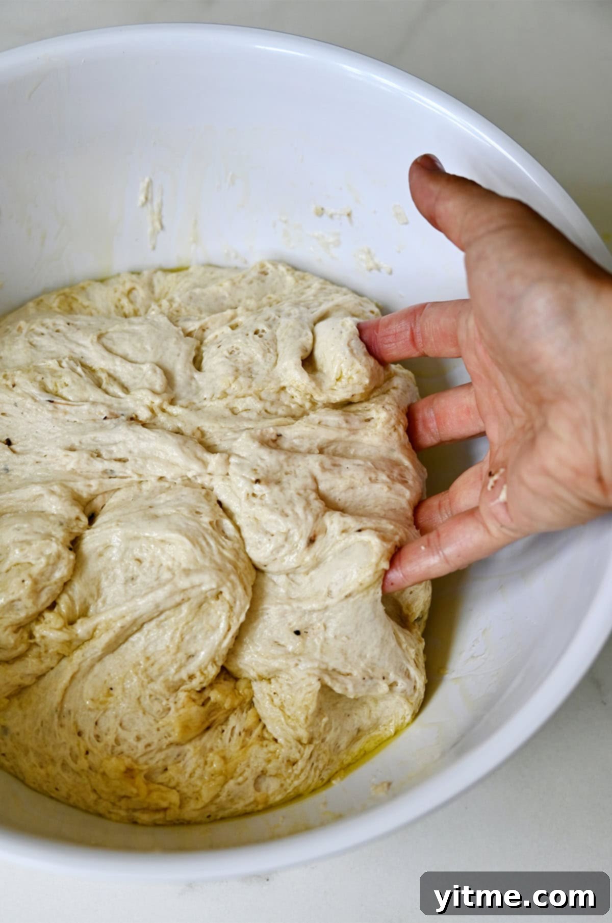 A hand gently folds dough over itself a couple of times in the bowl to deflate it.