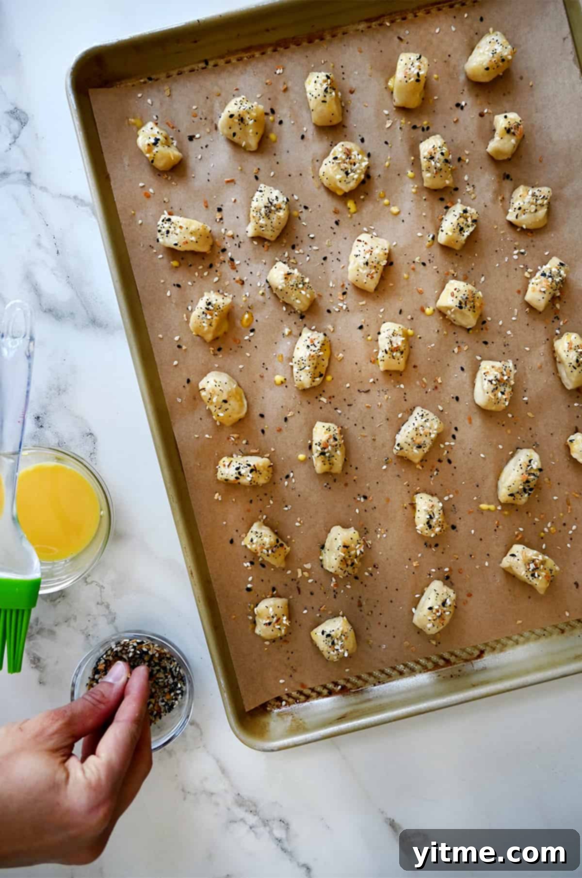 Unbaked pretzel bites, perfectly arranged on a parchment paper-lined baking sheet, glistening with egg wash and generously sprinkled with everything bagel seasoning, ready for the oven.