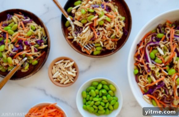 Easy ramen noodle salad artfully arranged in various sized bowls, accompanied by smaller bowls of shelled edamame, slivered almonds, and shredded carrots for garnish, highlighting its freshness and appeal.
