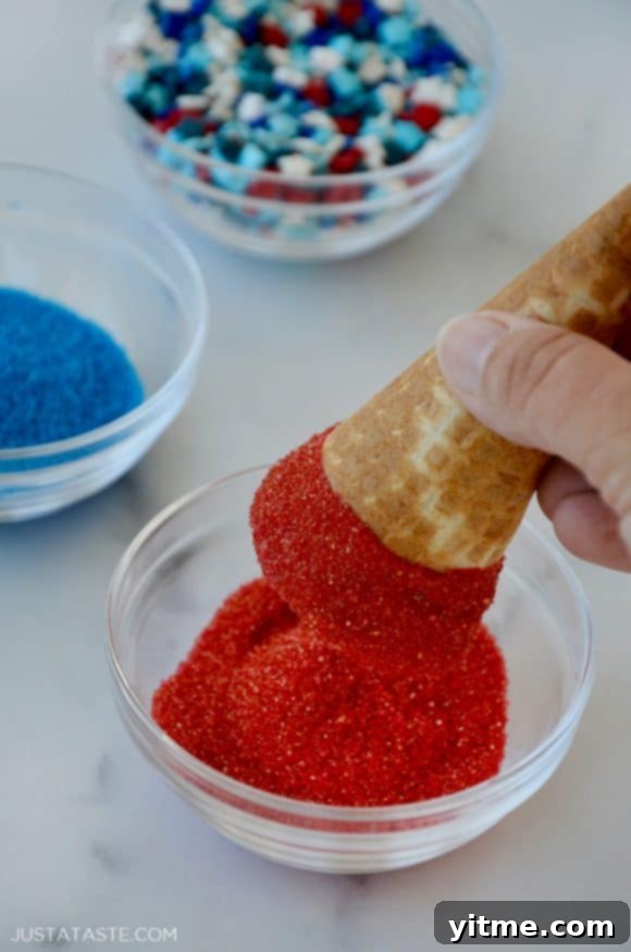 Hand holding waffle cone being dipped in red sprinkles