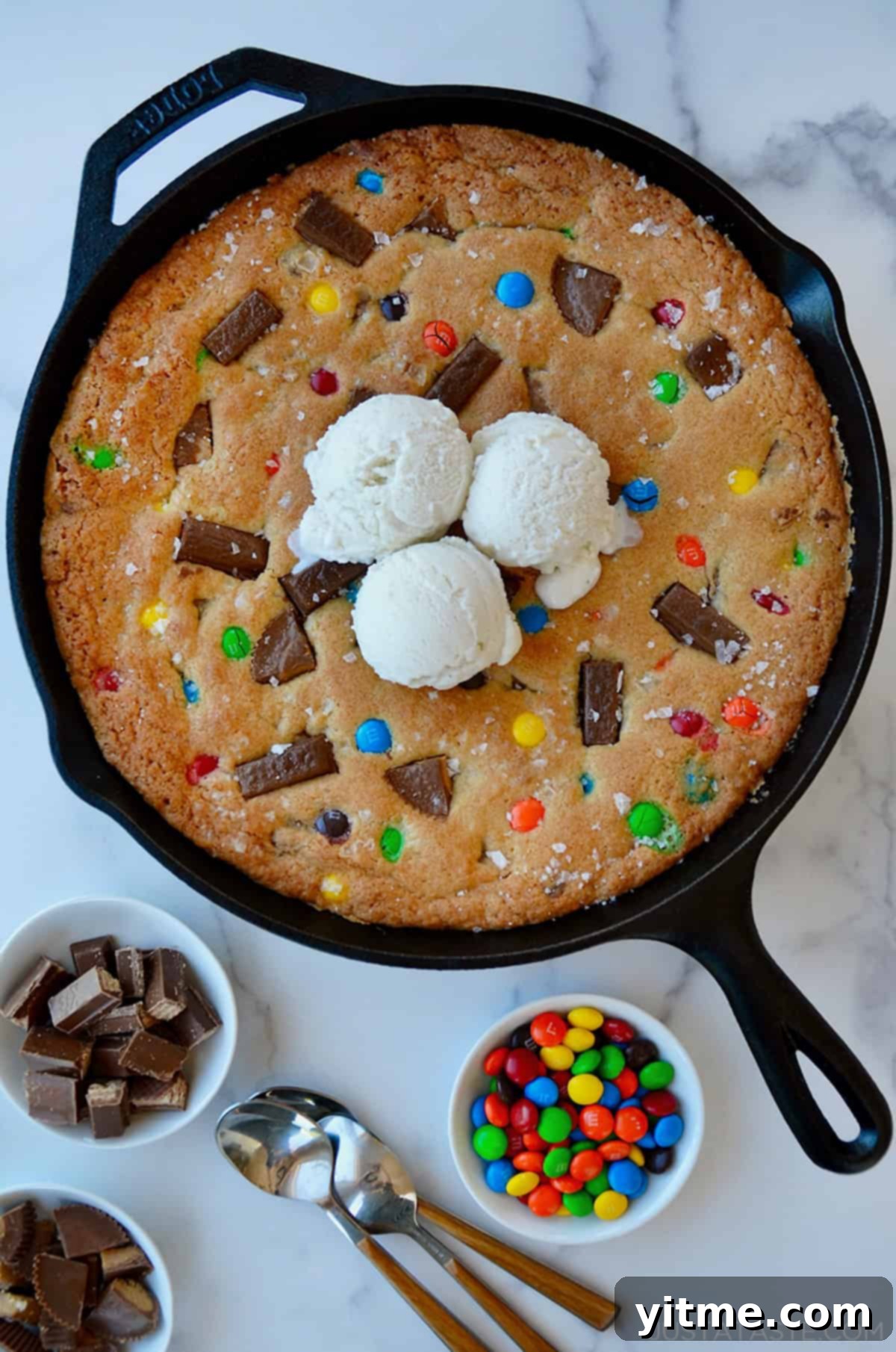 Leftover Halloween Candy Skillet Cookie topped with vanilla ice cream next to small bowls containing chocolate candy.
