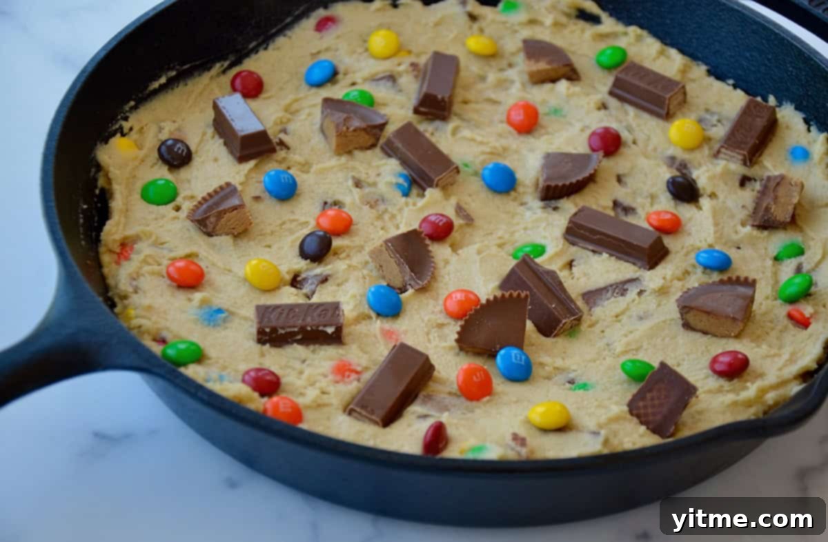 Cast iron skillet containing unbaked cookie dough topped with chopped candy.