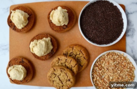 A cutting board containing cookies, ice cream and toppings for ice cream sandwiches