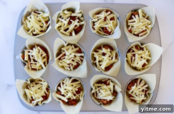 Top-down view of a muffin tin filled with unbaked lasagna cups, showcasing the layered ingredients before baking