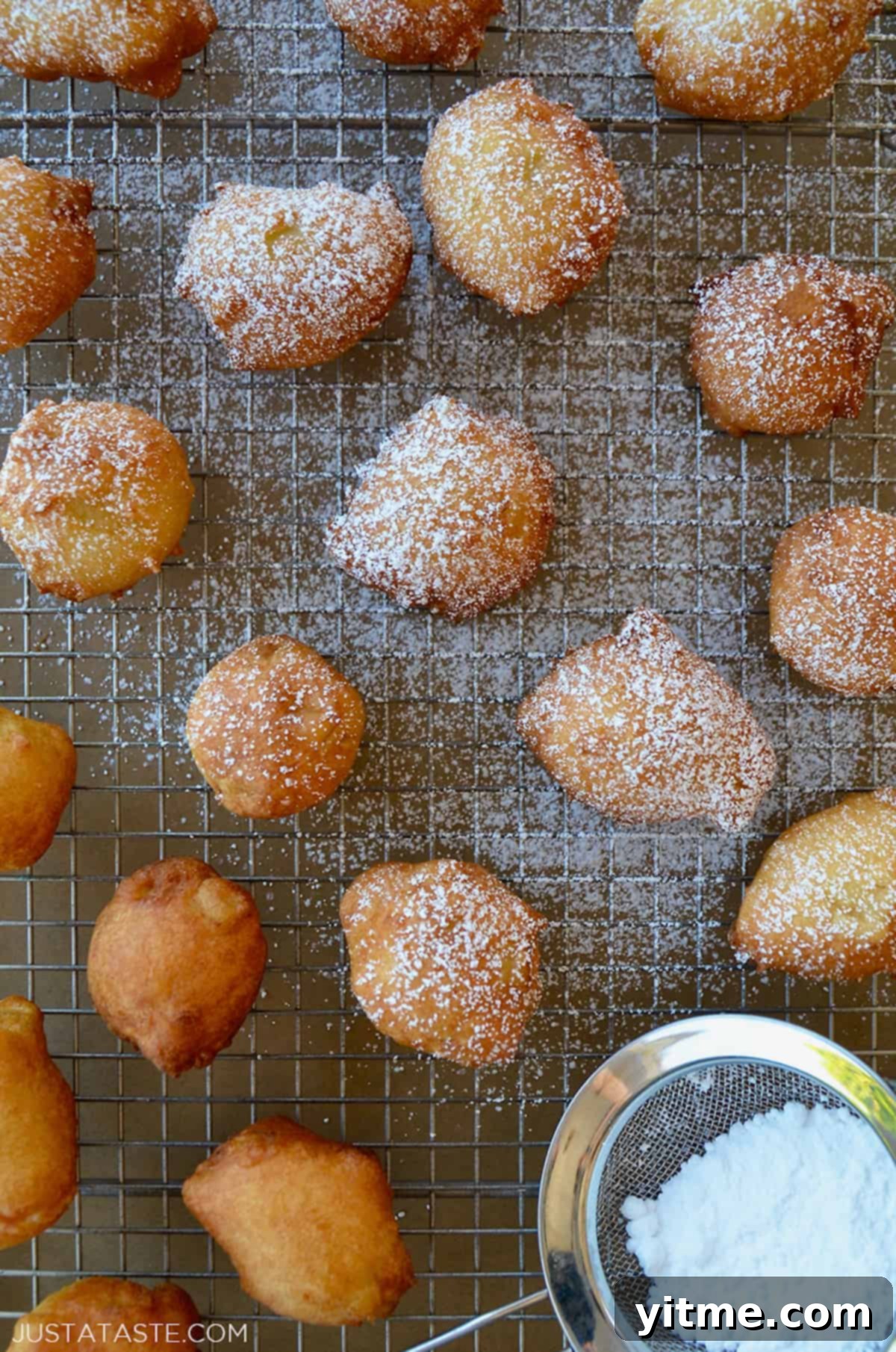 Whip Up Apple Fritters in 30 Minutes 3 Apple fritter doughnut holes dusted with powdered sugar on a wire rack.