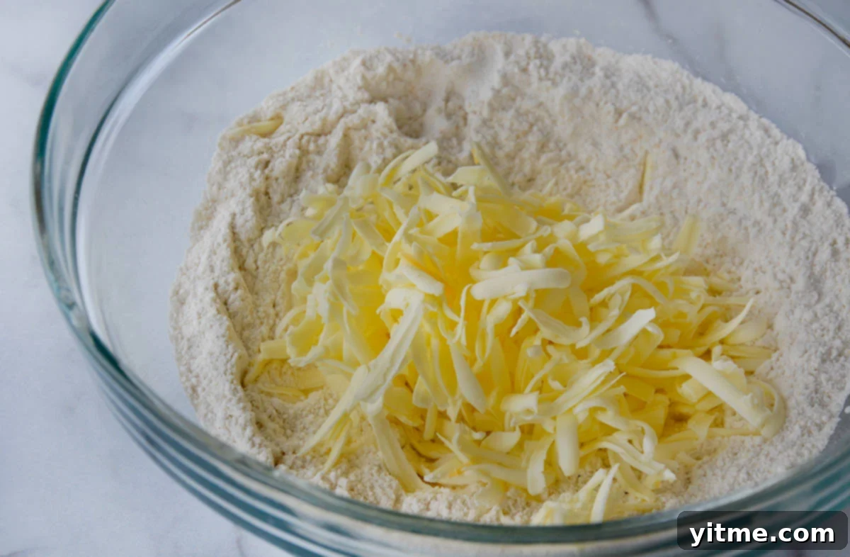 Irresistible Cheddar Biscuits 4 A glass bowl holds grated butter on top of flour, ready to be mixed into the biscuit dough.