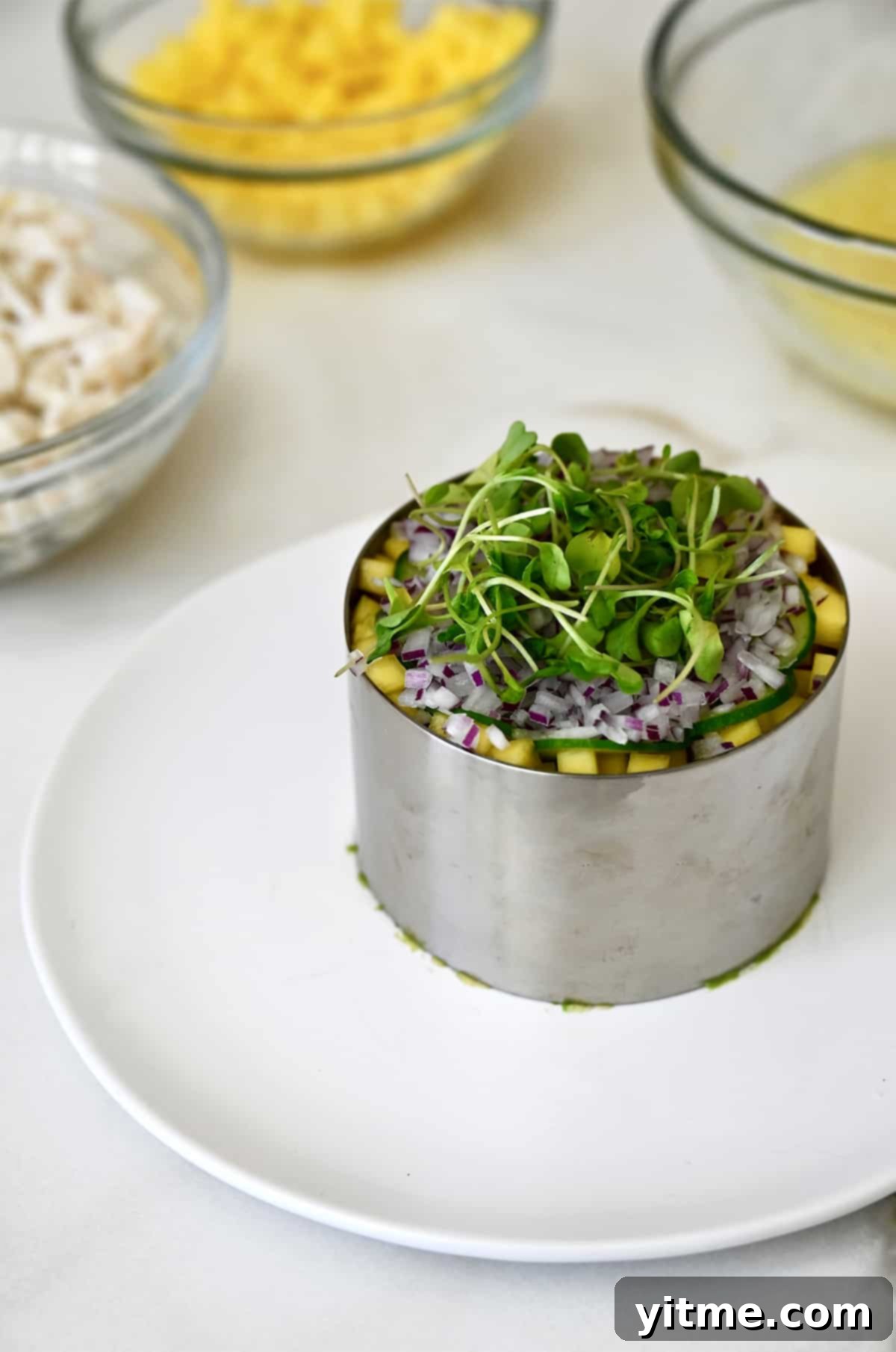 A ring mold showcasing the vibrant layers of mango, red onion, and microgreens within a crab stack, pre-drizzle.