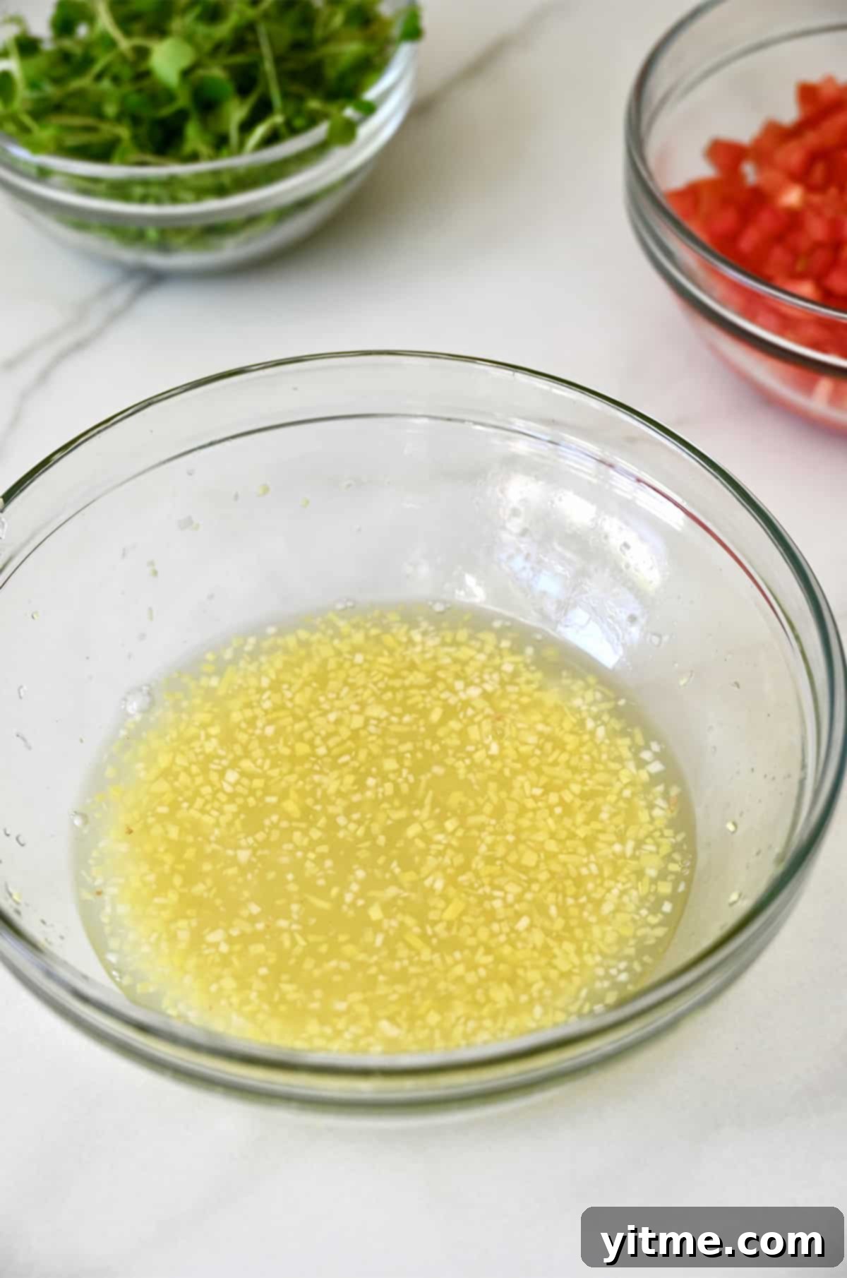 A glass bowl of zesty ginger-lime dressing nestled beside fresh microgreens and diced tomatoes, prepared for the crab stacks.