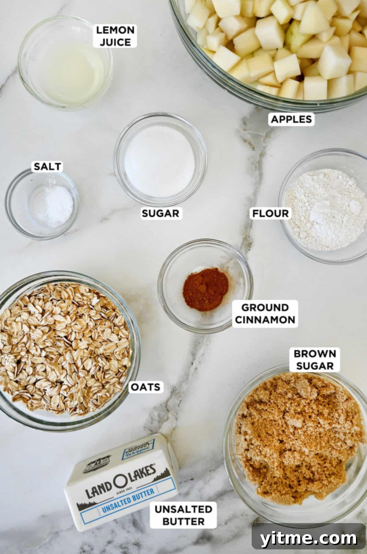Pear crisp ingredients in glass bowls, including brown sugar, oats, flour, ground cinnamon, diced apples and pears, butter, and sugar.