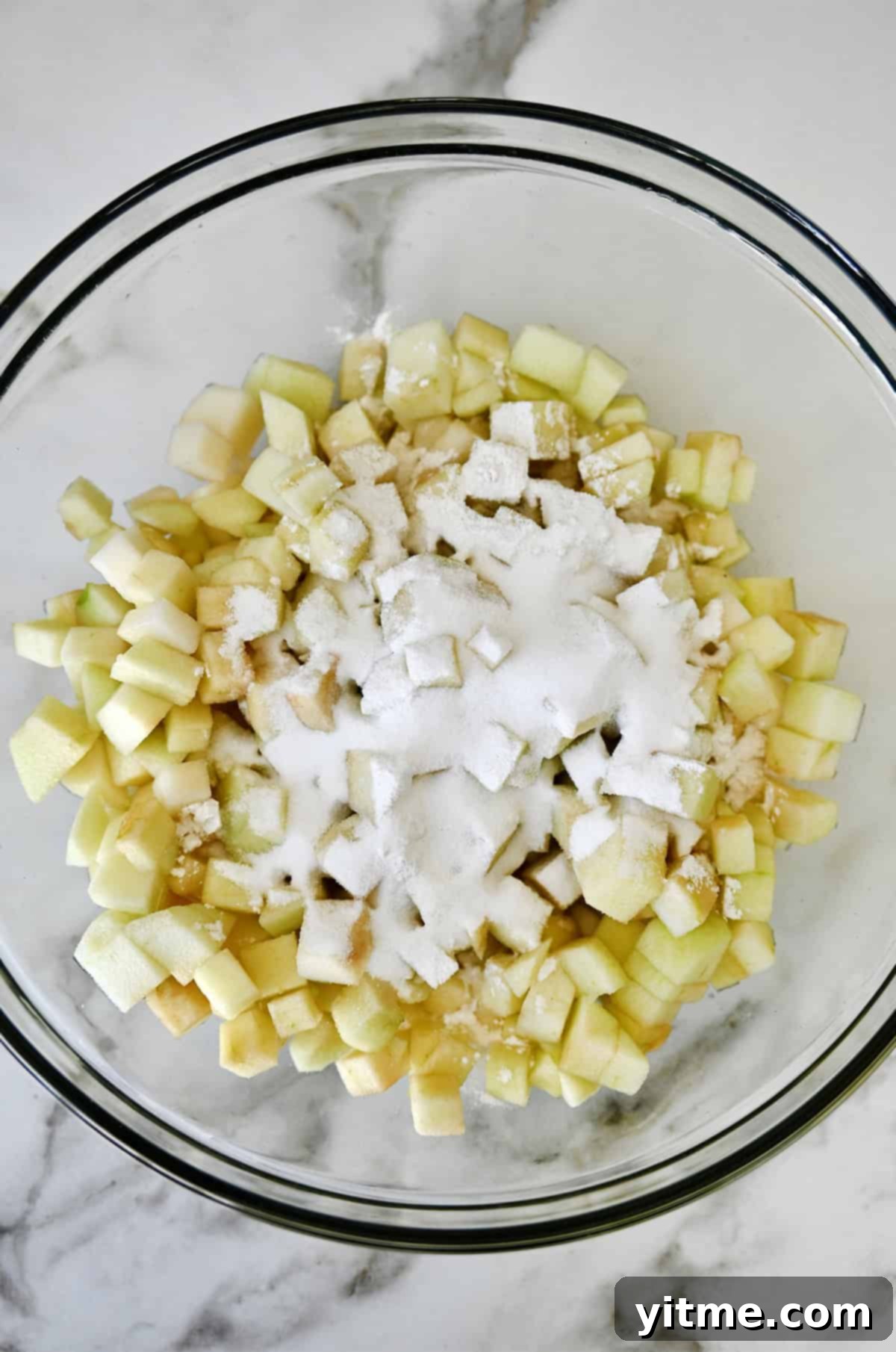 Diced apples and pears covered with flour, sugar and lemon juice in a glass bowl.