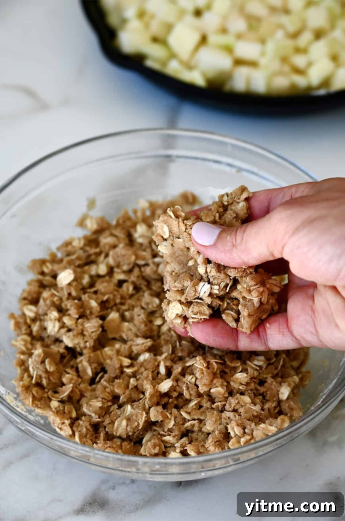 A hand holds some crisp topping to show the crumbly texture of the mixture.