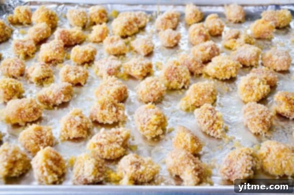 Unbaked crispy chicken bites atop a baking sheet lined with foil, ready for the oven