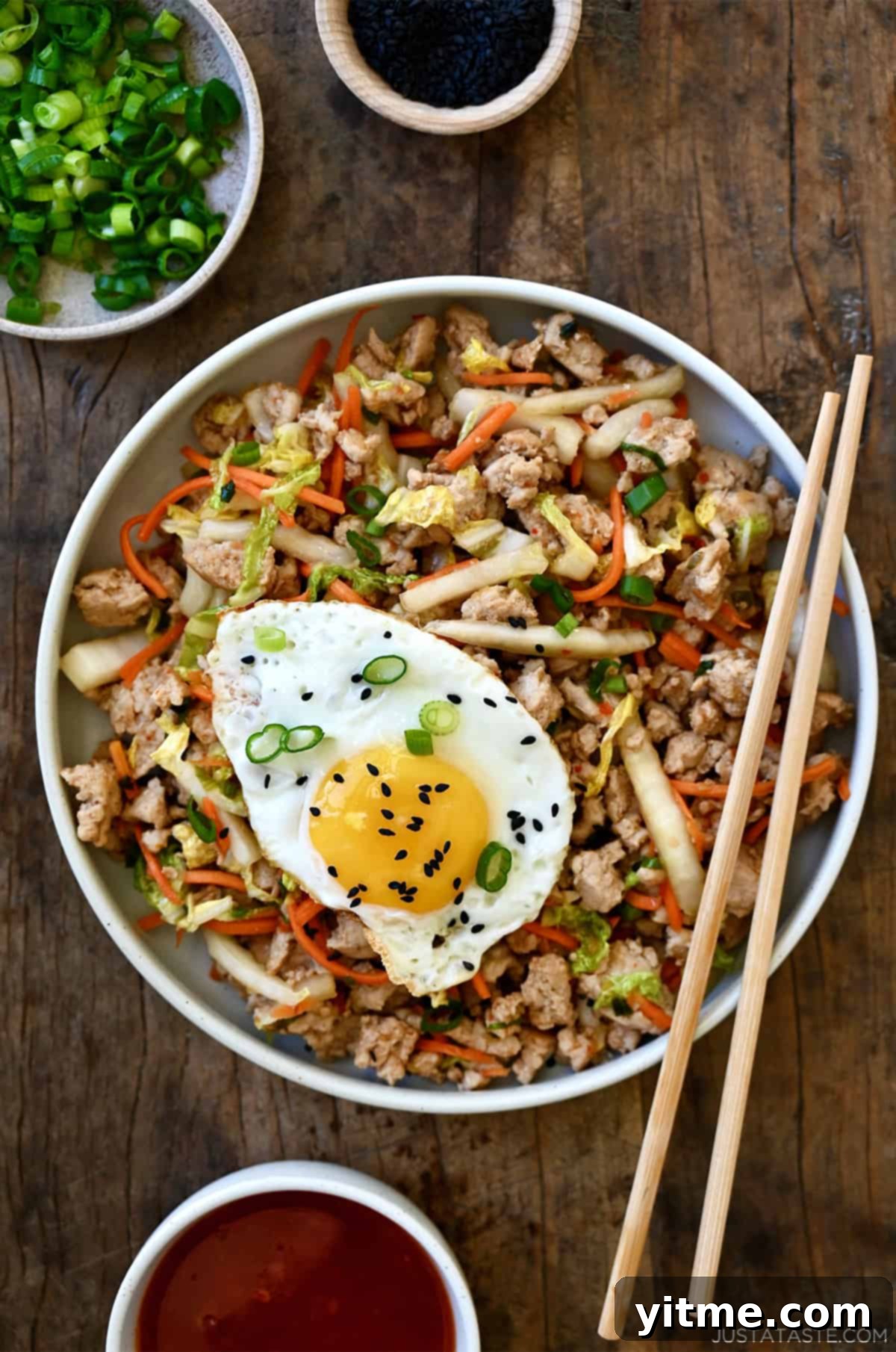 Egg roll in a bowl with ground meat, shredded cabbage and carrots, topped with a fried egg and black sesame seeds.