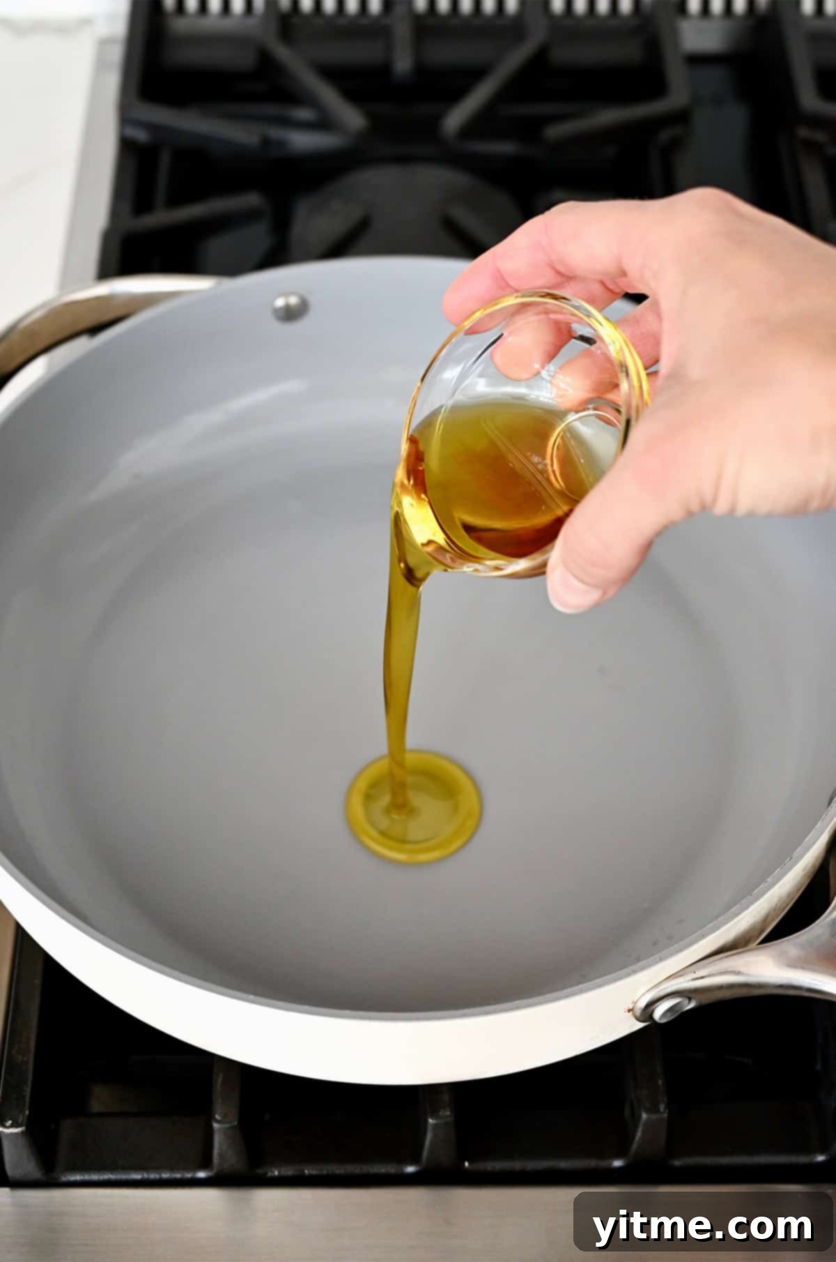 Adding sesame oil from a small bowl into a hot skillet.