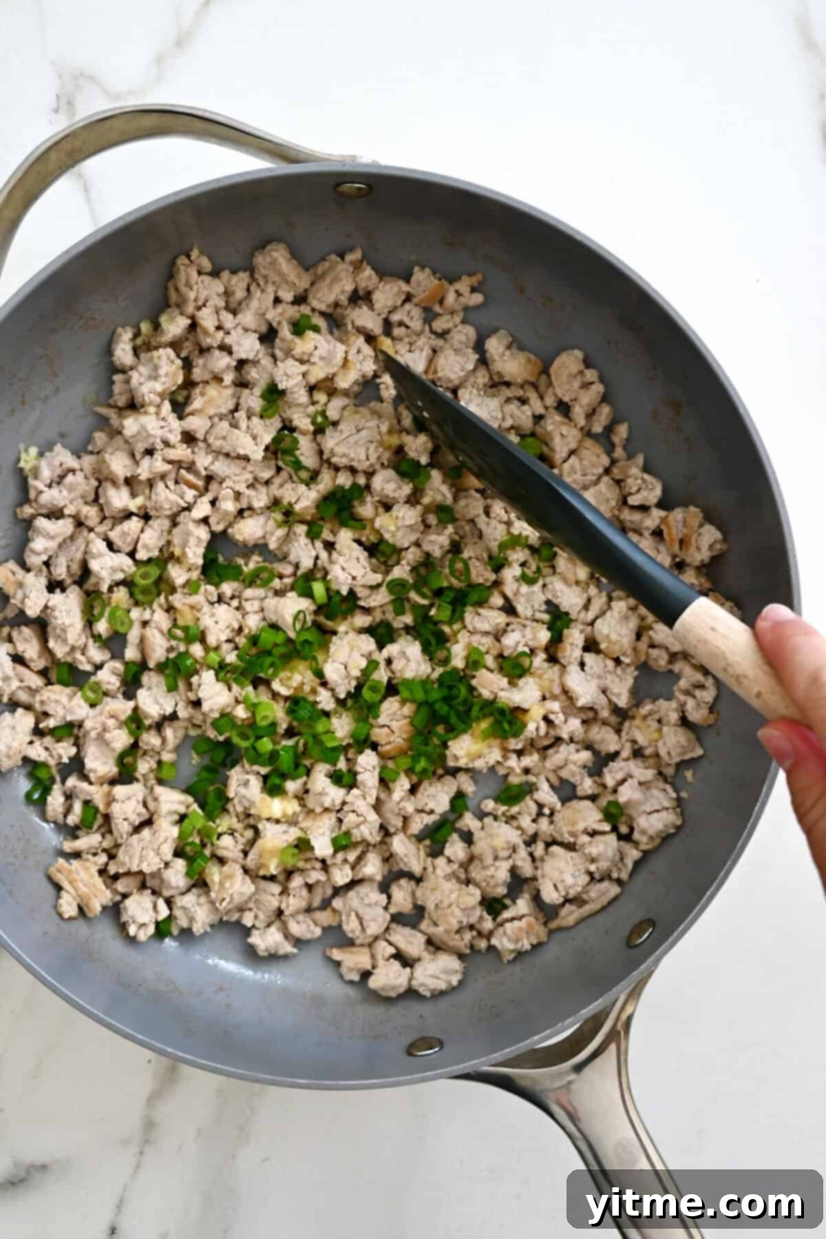 Chopped scallions, minced garlic and ginger atop browned meat in a skillet.