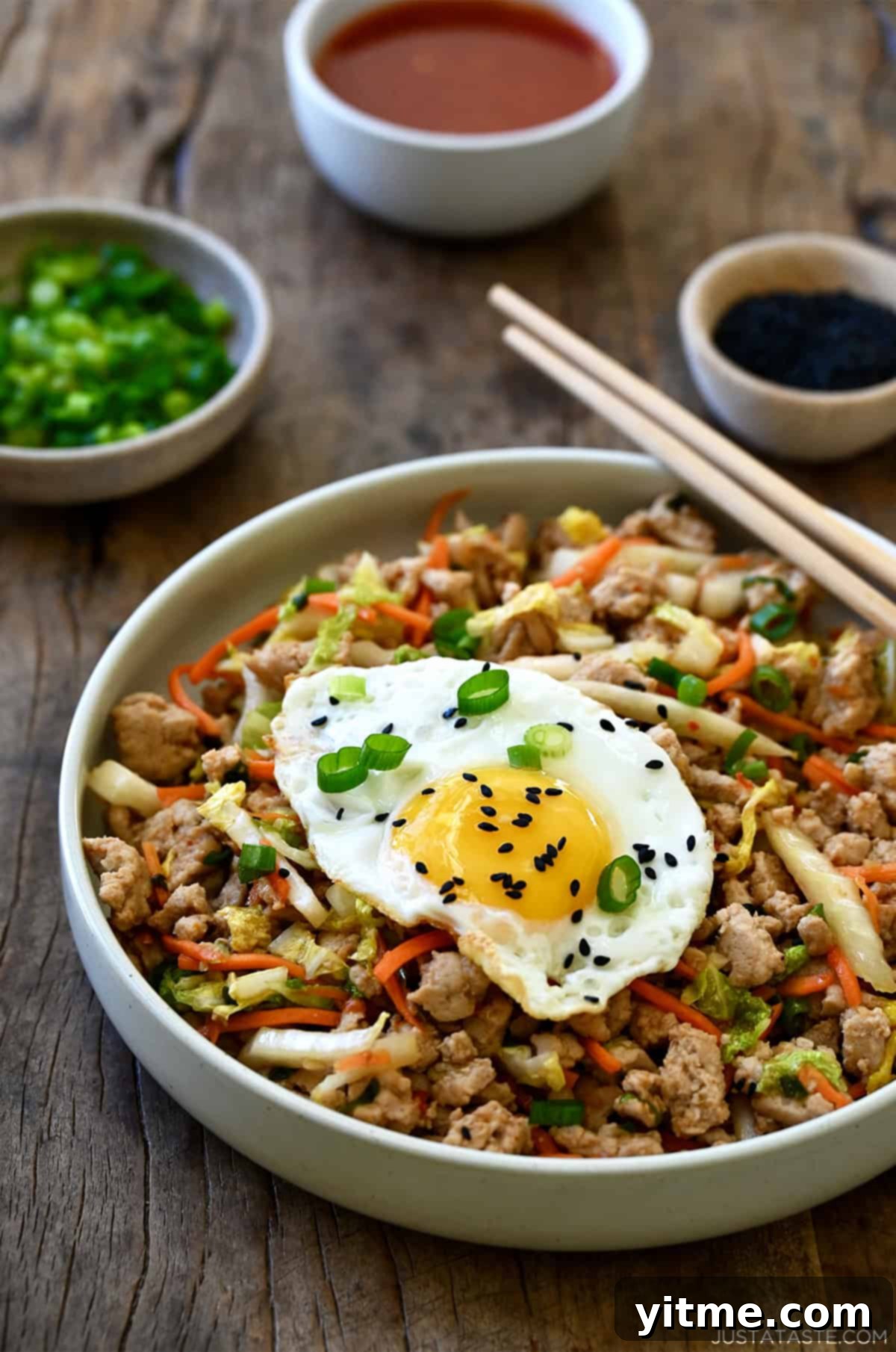 Healthy egg roll in a bowl, including ground turkey, coleslaw mix and soy sauce, topped with a fried egg and black sesame seeds.