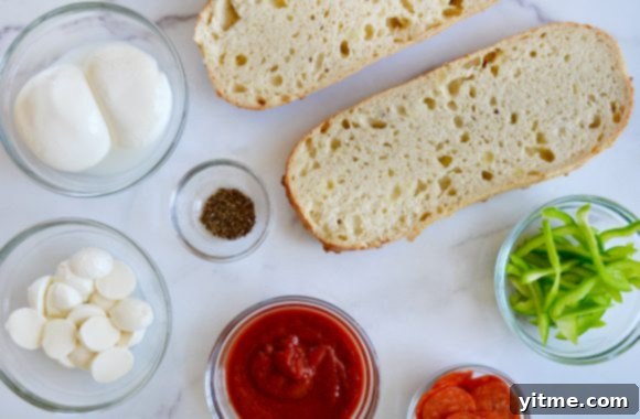 Ingredients for French Bread Pizza laid out in bowls: halved bread, green peppers, pepperoni, marinara sauce, mozzarella, Italian seasoning, and fresh burrata cheese.