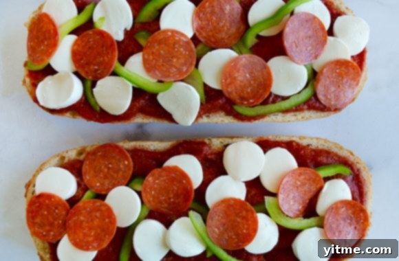 Close-up of unbaked French bread pizza, showcasing the vibrant green peppers, pepperoni, and melty mozzarella cheese.