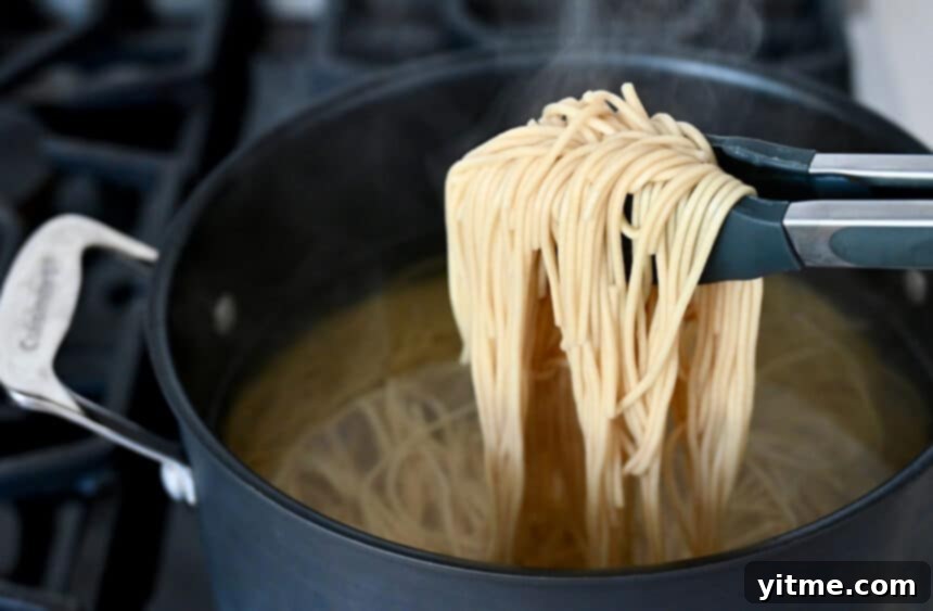 Tongs holding noodles over a pot filled with water