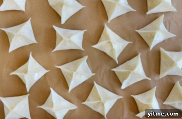 Unbaked crab rangoon, perfectly folded and arranged in a single layer on parchment paper-lined baking sheet, ready for the oven