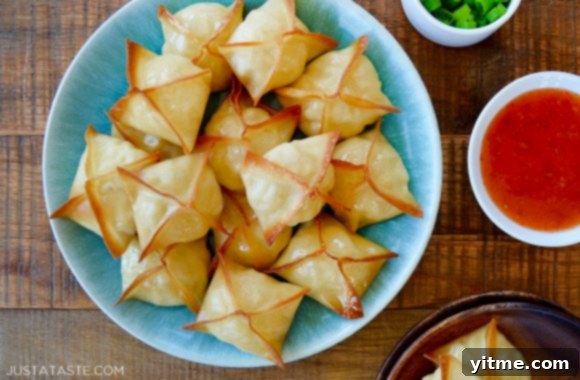 Easy baked crab rangoon piled on a blue serving plate next to a small bowl of vibrant sweet and sour sauce for dipping