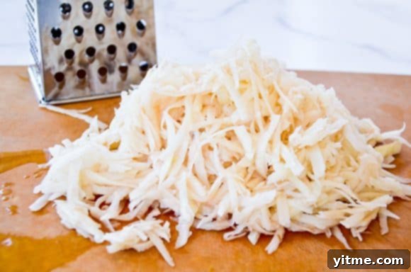 Shredded russet potatoes on a cutting board with a box grater