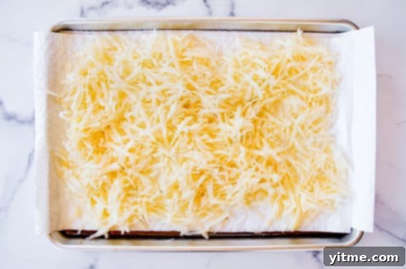 Shredded potatoes spread on a paper towel-lined baking sheet