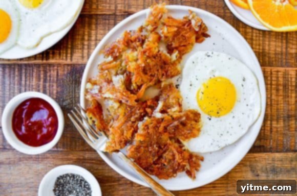 Crispy hash browns on a plate with a fried egg, pepper, and ketchup