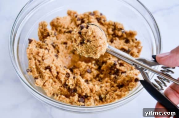 Peanut Butter Bliss Bites 4 Hand using a small ice cream scoop to portion out the no-bake mixture into a clear bowl