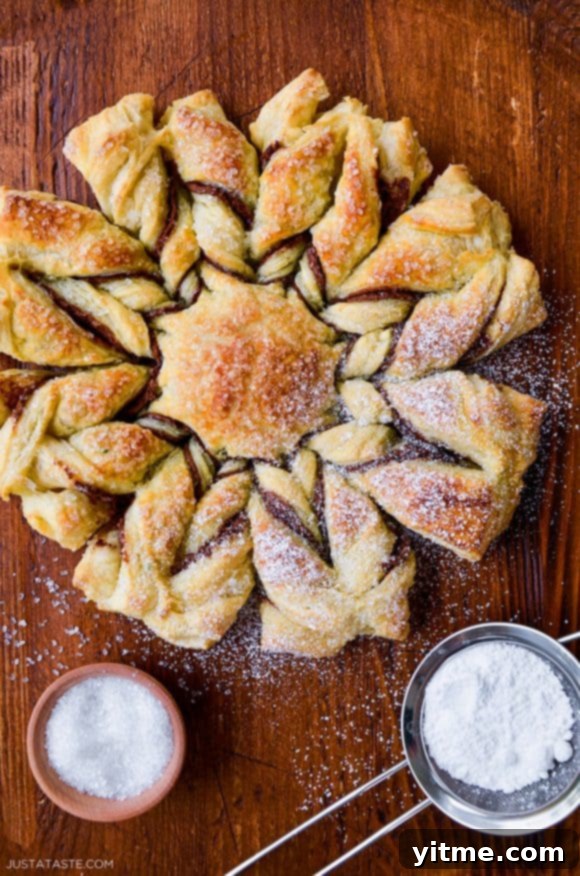 Effortless Snowflake Pastry Delight 11 A top-down view of a puff pastry dessert dusted with confectioners' sugar, showing its golden-brown color.