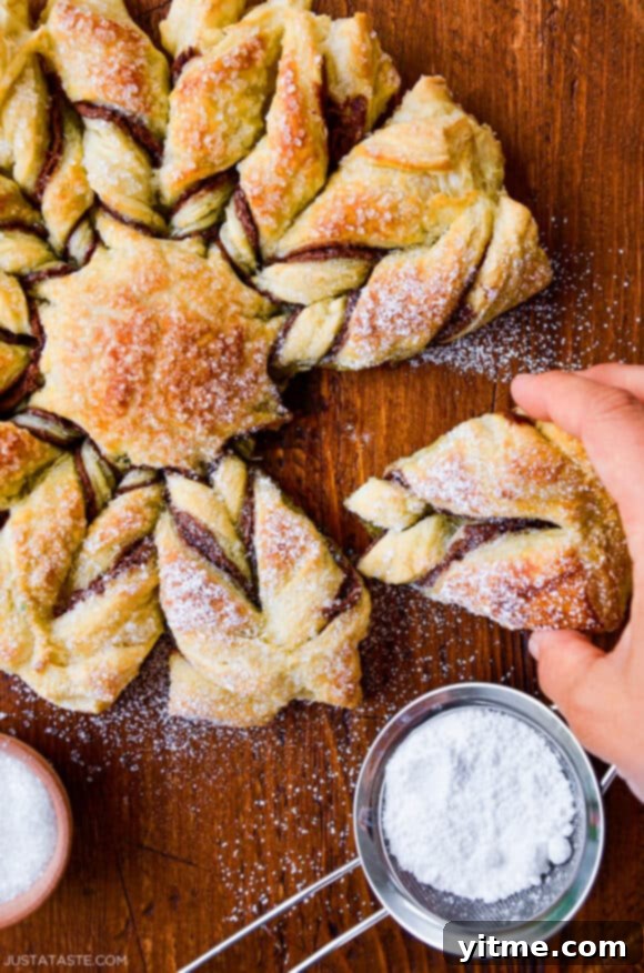 Effortless Snowflake Pastry Delight 3 Hands gently pulling apart a section of the puff pastry snowflake, revealing the layers of pastry and filling.