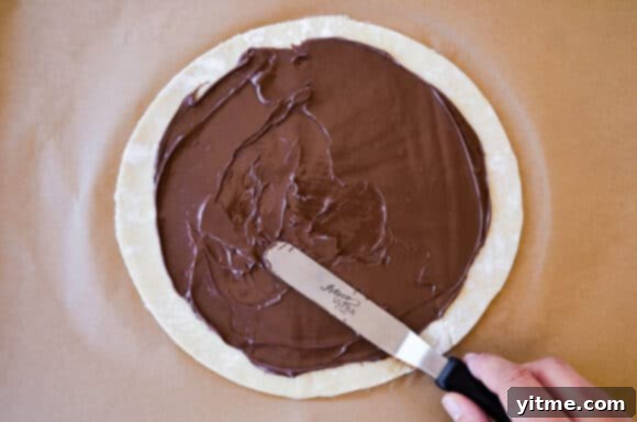 Effortless Snowflake Pastry Delight 5 Puff pastry topped with a generous layer of Nutella, ready to be covered with another sheet of pastry.