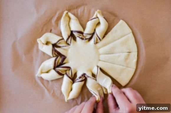 Effortless Snowflake Pastry Delight 7 Hands twisting the sections of puff pastry to create the snowflake shape, demonstrating the twisting technique.