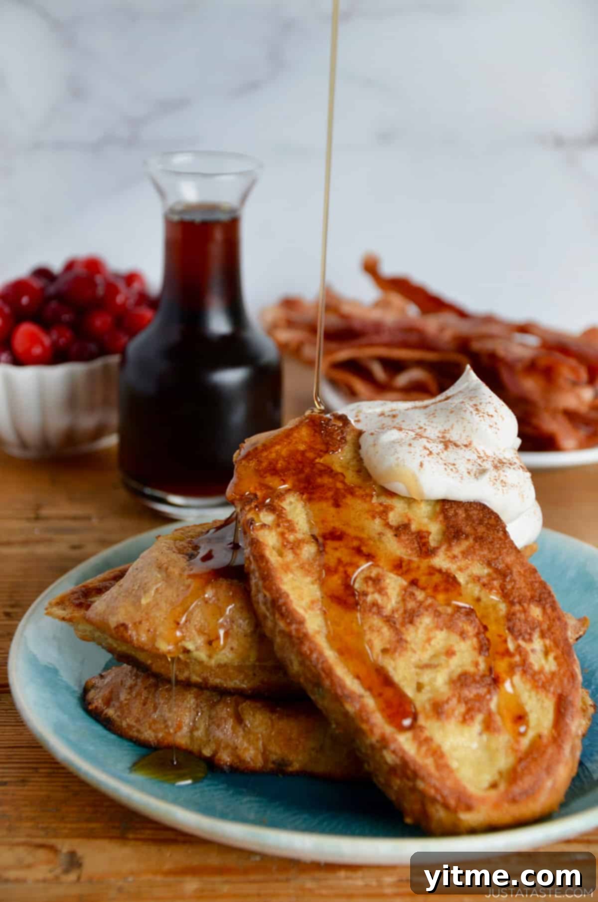 Slices of eggnog French toast topped with whipped cream and cinnamon, drizzled with maple syrup.
