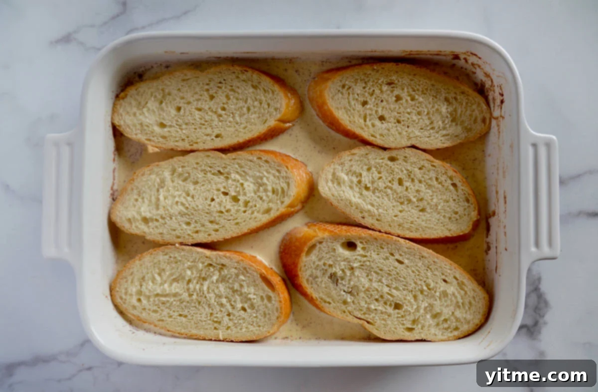 Slices of bread soaking in custard in a rectangular baking dish.