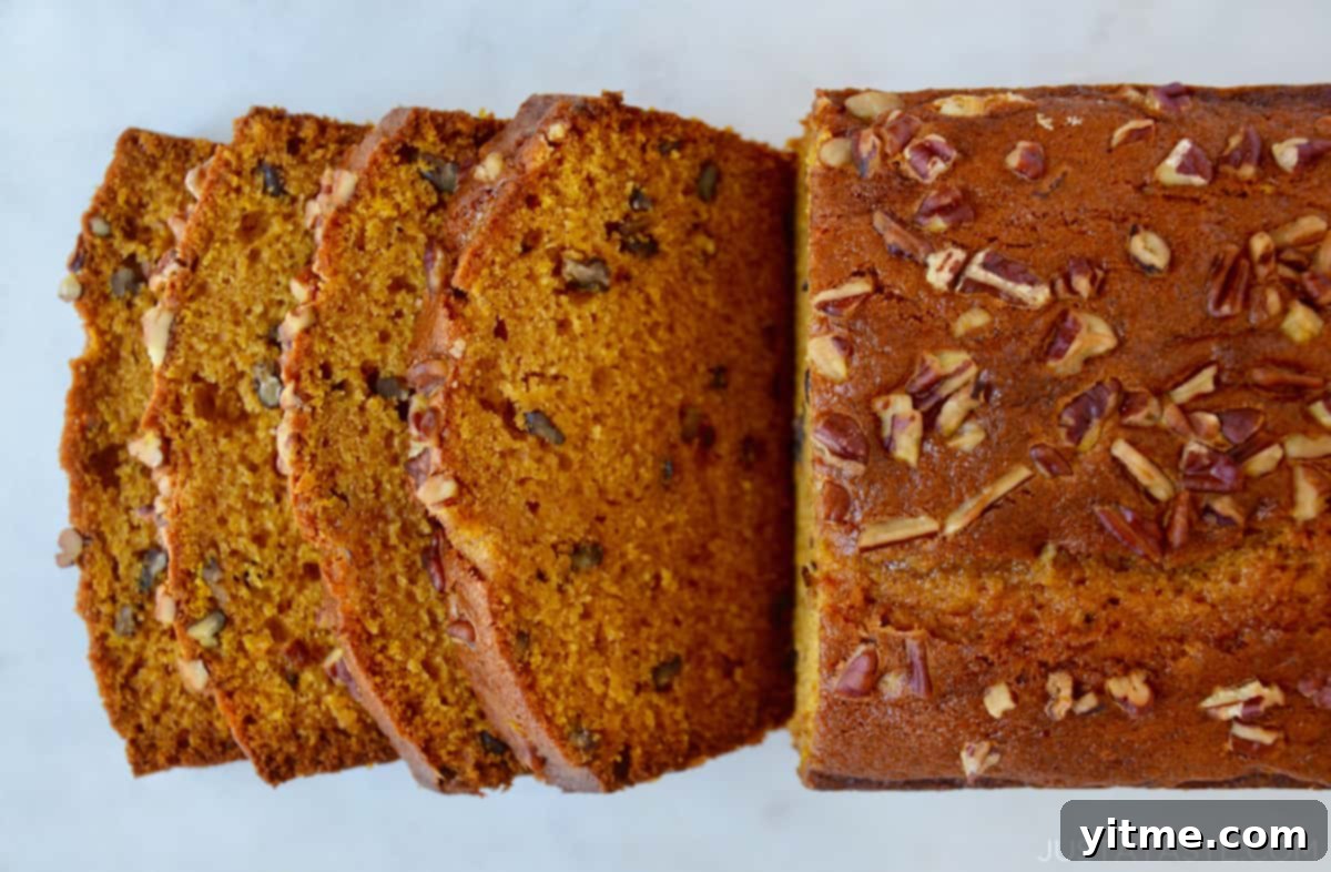 Ultimate Autumn Pumpkin Bread 5 A whole loaf of pumpkin bread adorned with chopped pecans, with several slices fanned out, emphasizing its inviting, moist interior.