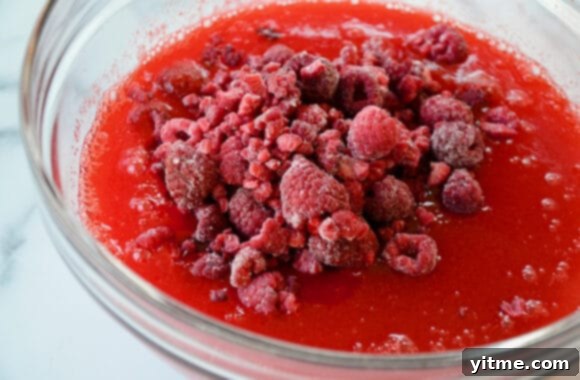 A glass bowl filled with the raspberry Jell-O and scattered frozen raspberries