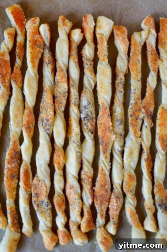 A close up of cheesy puff pastry twists on a baking sheet lined with parchment paper. Cheese straws are an excellent addition to any charcuterie board.