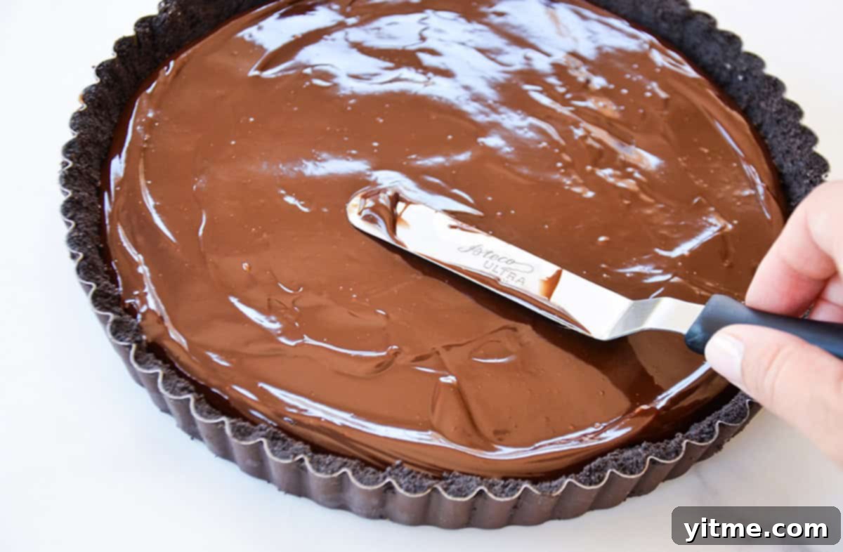 Effortless Raspberry Chocolate Tart 5 An offset spatula spreading the smooth chocolate ganache evenly over the chocolate cookie crust.