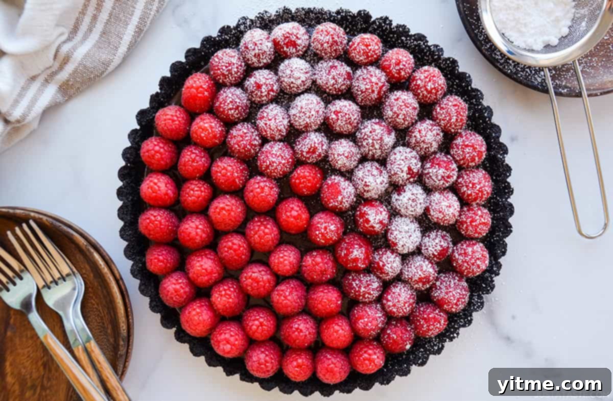 Effortless Raspberry Chocolate Tart 7 A chocolate tart adorned with fresh raspberries, half dusted with a delicate layer of powdered sugar.