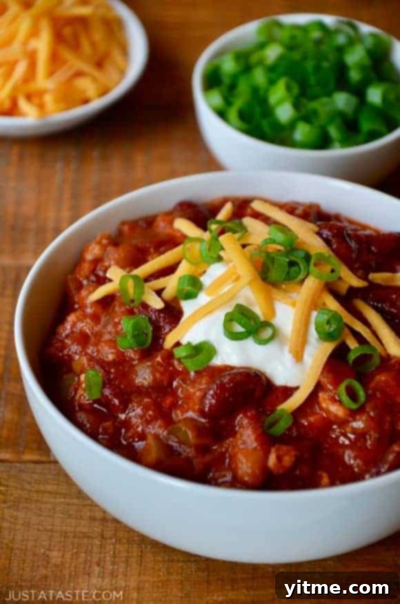A white bowl containing Turkey Taco Stew topped with sour cream, cheese and scallions