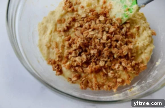 Spatula in glass bowl containing muffin batter with granola