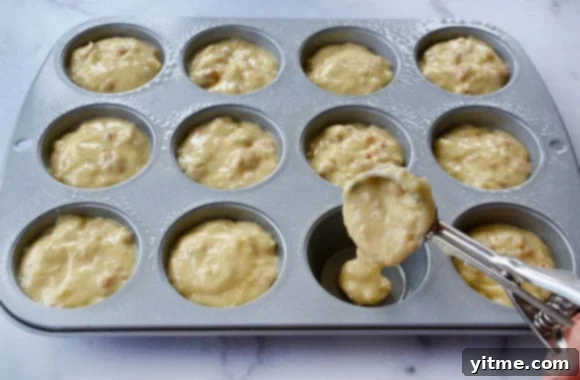 Ice cream scoop filling muffin tin with batter