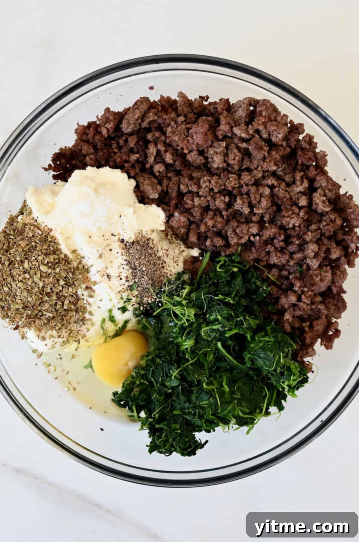 Cooked ground beef, spinach, egg, ricotta cheese and seasonings in a large glass bowl.