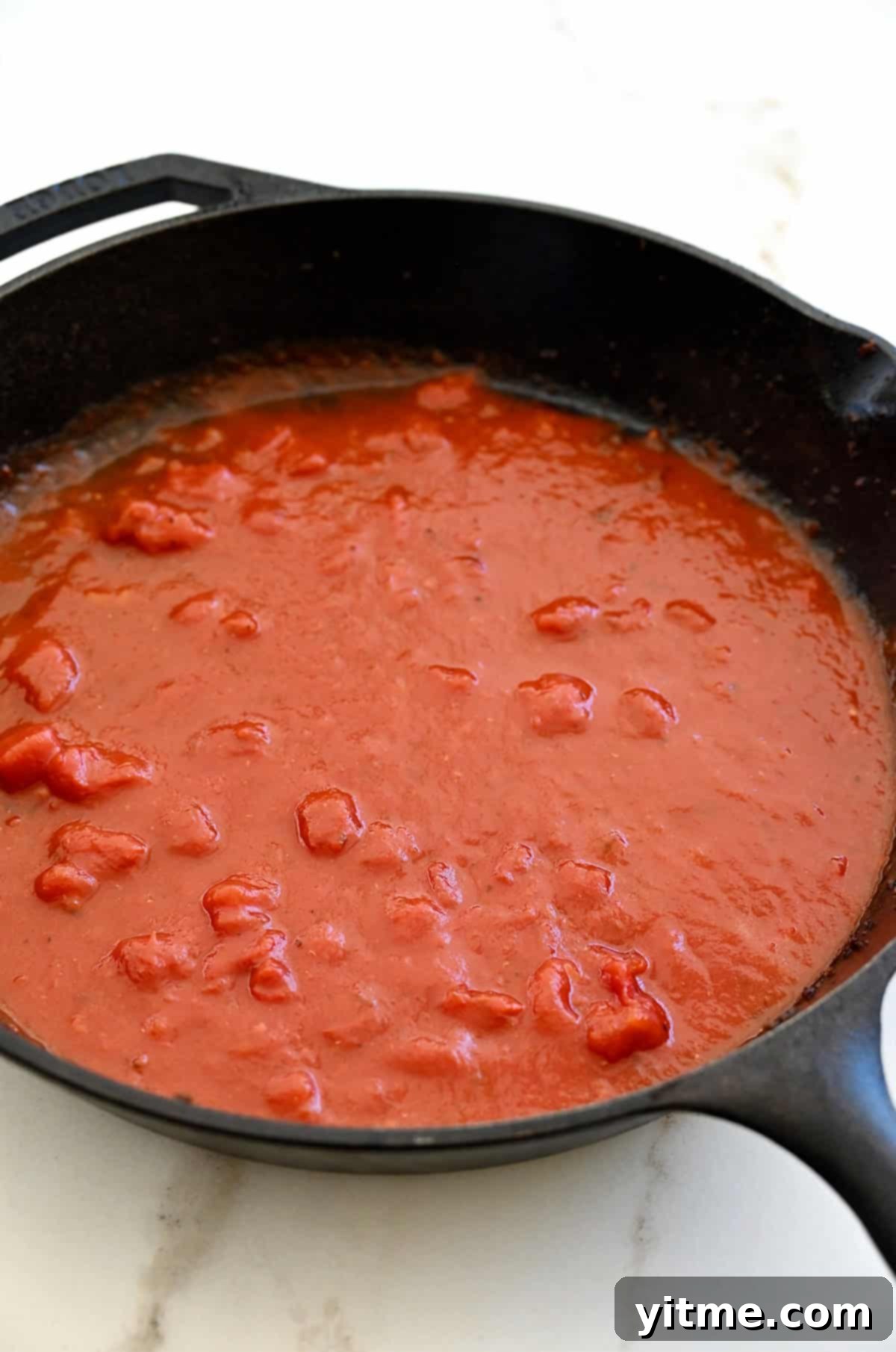 A thin layer of marinara sauce in a cast iron skillet.