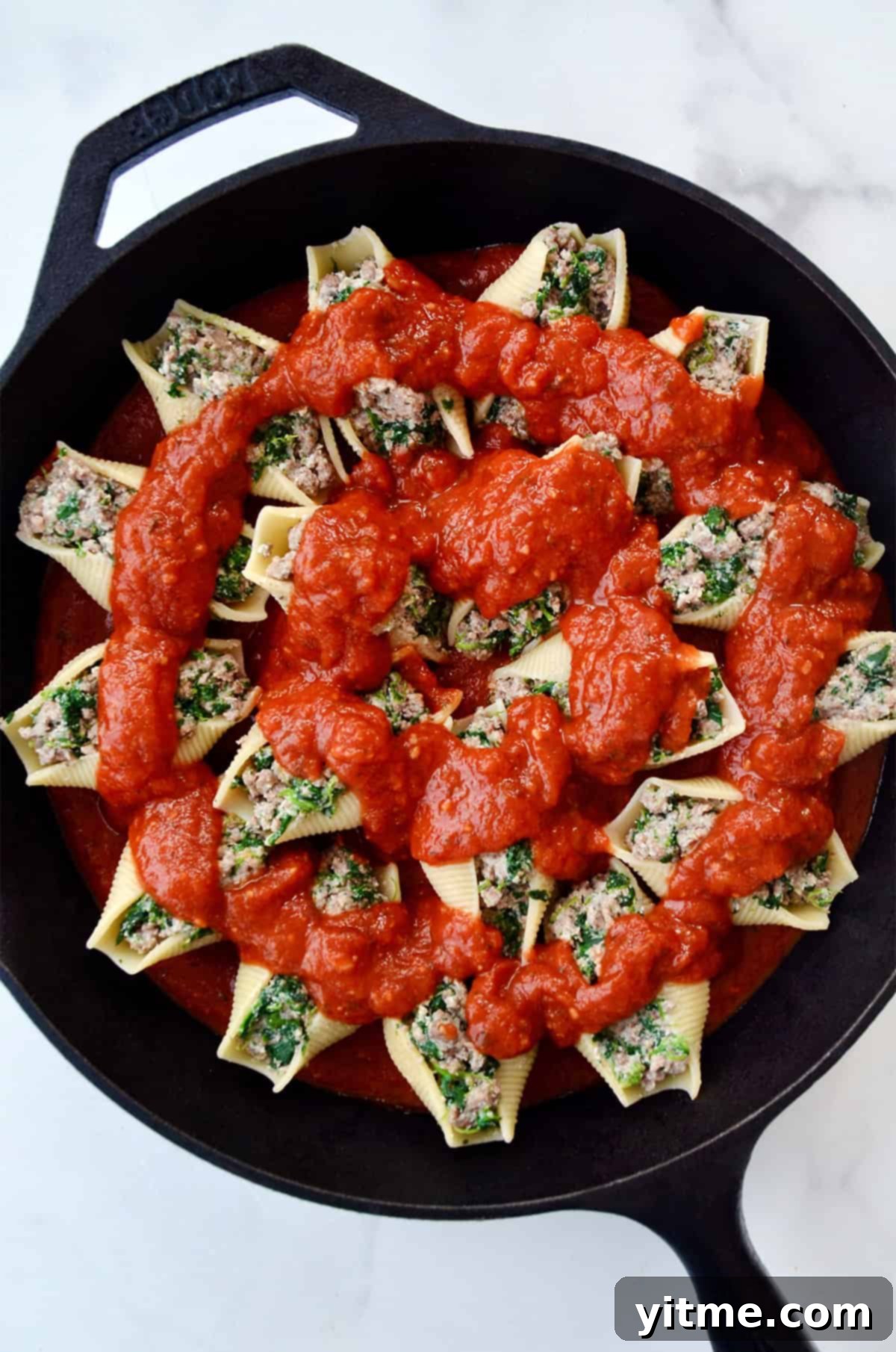 Beef, ricotta and spinach stuffed shells topped with marinara sauce in a cast iron skillet.