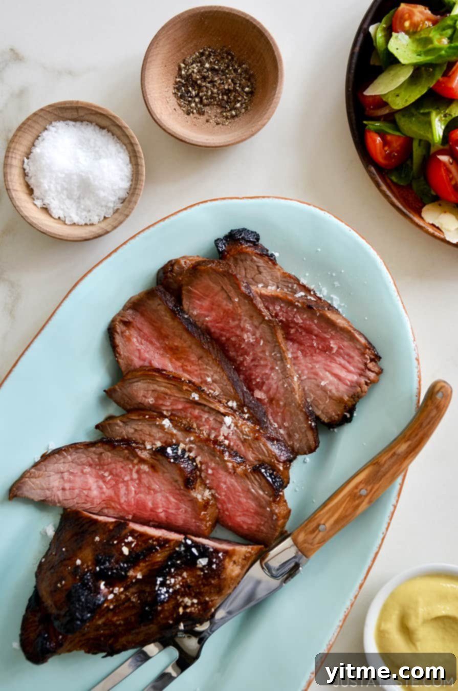 Sliced tri-tip on a blue serving platter with salt and pepper