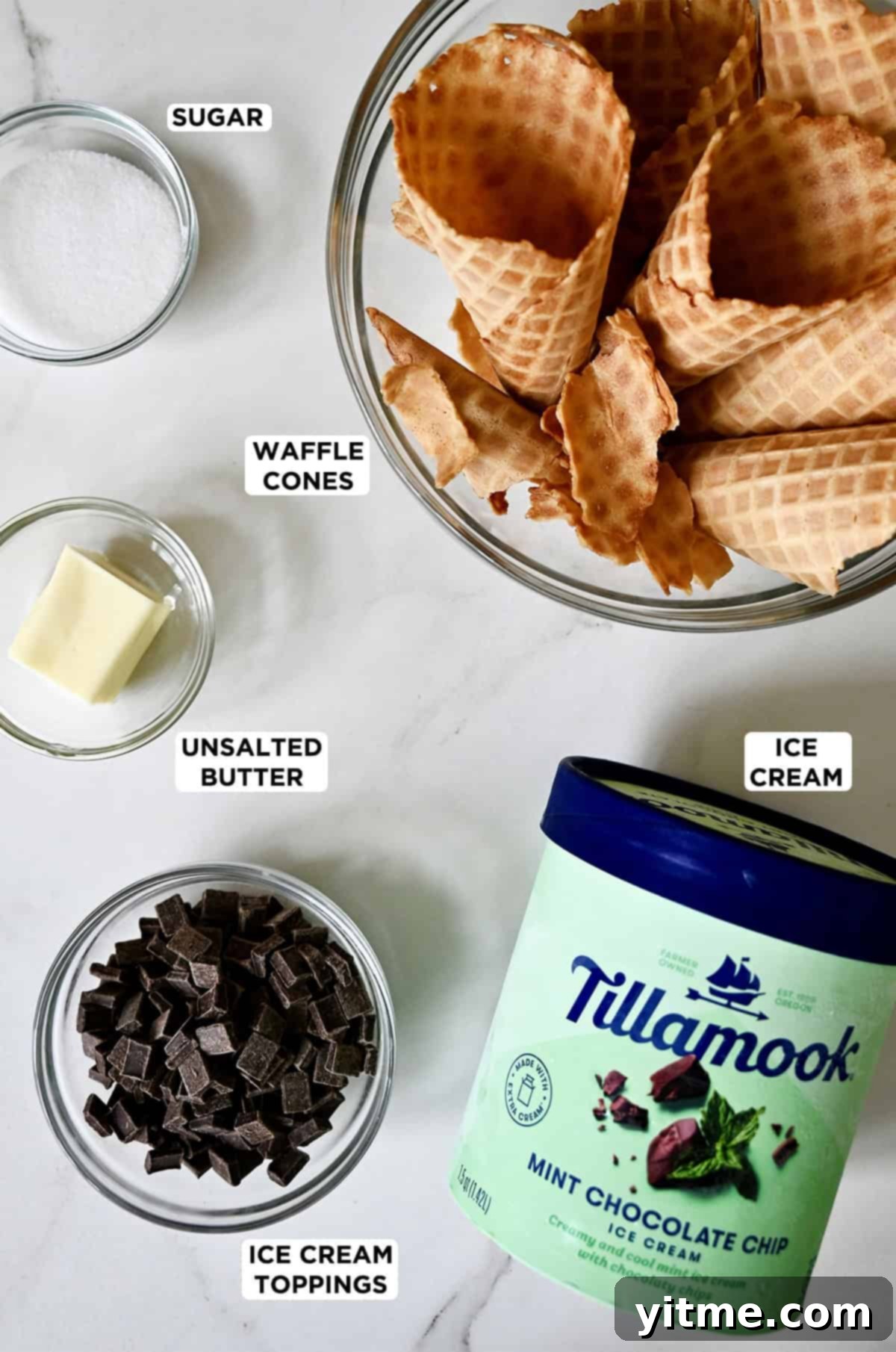 Mystery Ingredient Ice Cream Pie 4 A small tub of Tillamook mint chocolate chip ice cream next to glass bowls containing chocolate chunks, unsalted butter, sugar and finely crushed waffle cone pieces, showcasing the main ingredients.