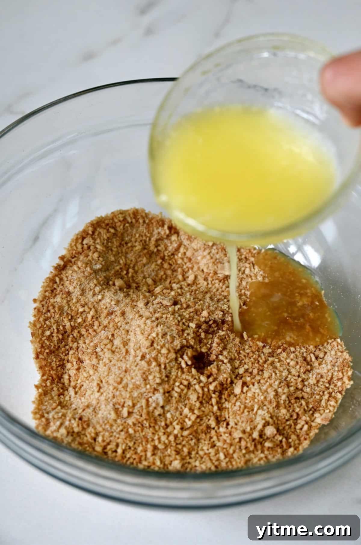 Mystery Ingredient Ice Cream Pie 7 Melted butter being poured from a small bowl atop waffle cone crumbs and sugar in a glass bowl, illustrating the crust mixture preparation.