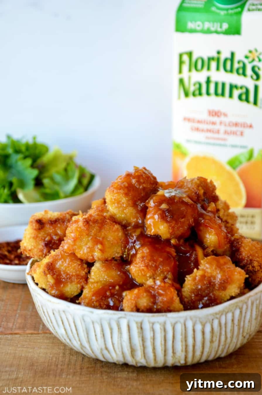 Crispy Citrus Chicken Bites 2 A white bowl containing baked orange chicken with a carton of Florida's Natural Orange Juice in the background